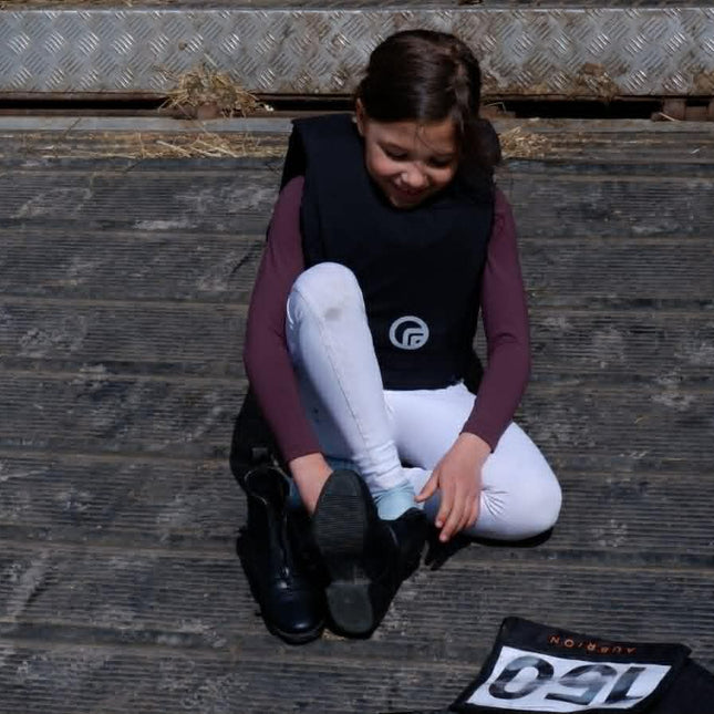 Person sitting on wooden steps with equestrian boots and a saddle pad.