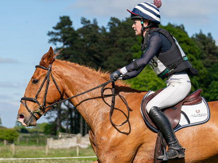 Person riding a brown horse in an outdoor setting with trees and clear sky.