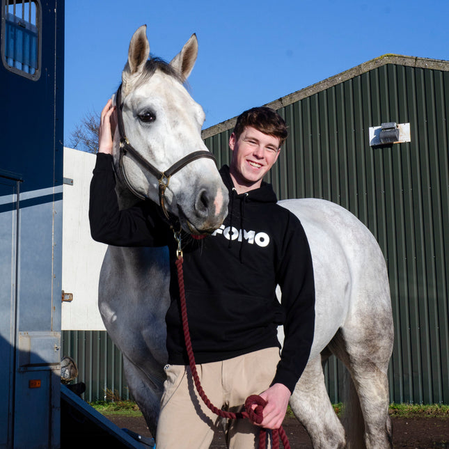 Man standing next to a white horse with a blue sky background