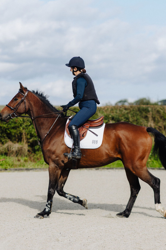 Person riding a brown horse on a paved area with greenery in the background