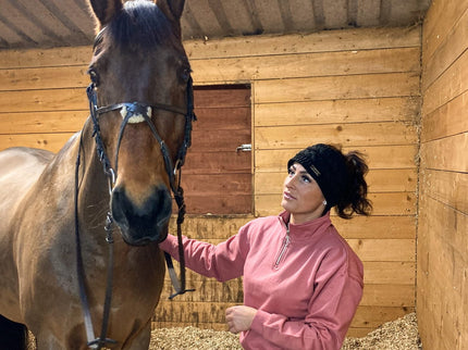 Woman in a pink jacket standing next to a horse in a stable.