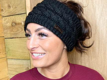 Woman wearing a black knit headband with a brand logo against a wooden background