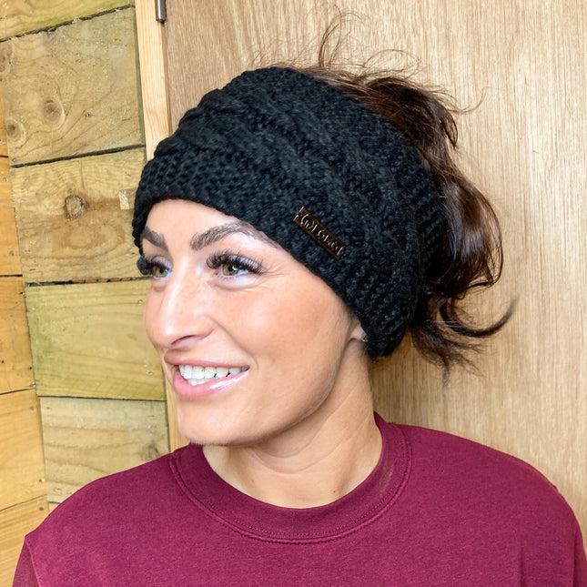 Woman wearing a black knit headband with a brand logo against a wooden background