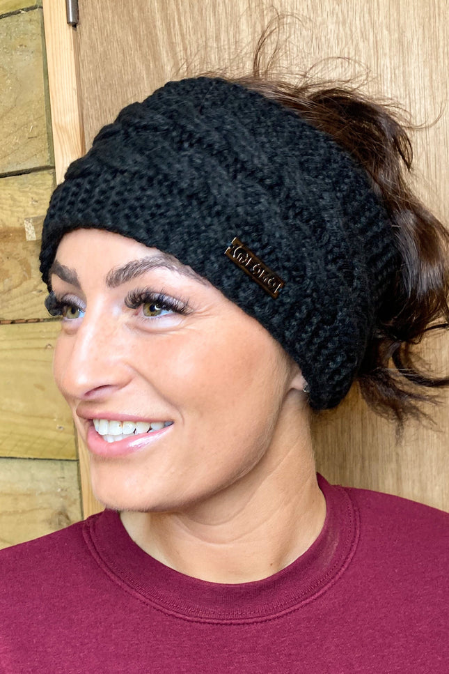 Woman wearing a black knit headband with a brand logo against a wooden background