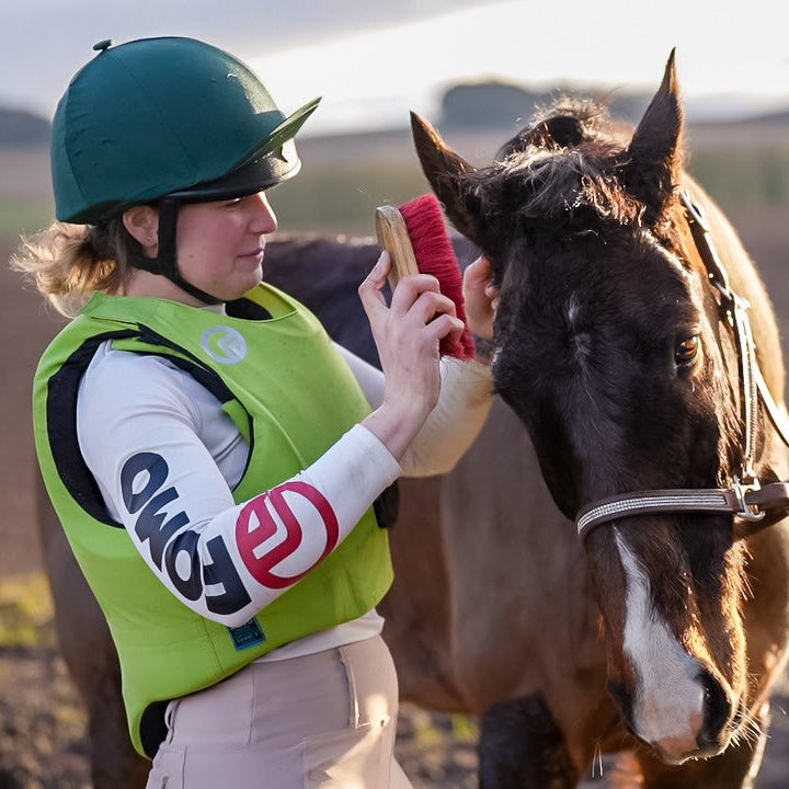 Person in equestrian gear interacting with a horse outdoors