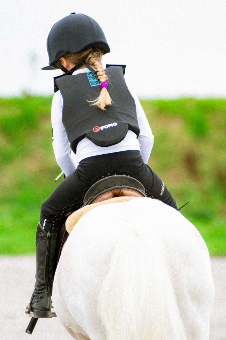 Little Gill riding a horse wearing a protective vest with a visible brand logo.