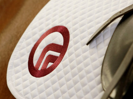 Close-up of a white saddle pad with a red logo on a horse.