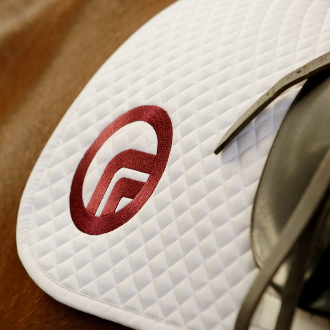 Close-up of a white saddle pad with a red logo on a horse.