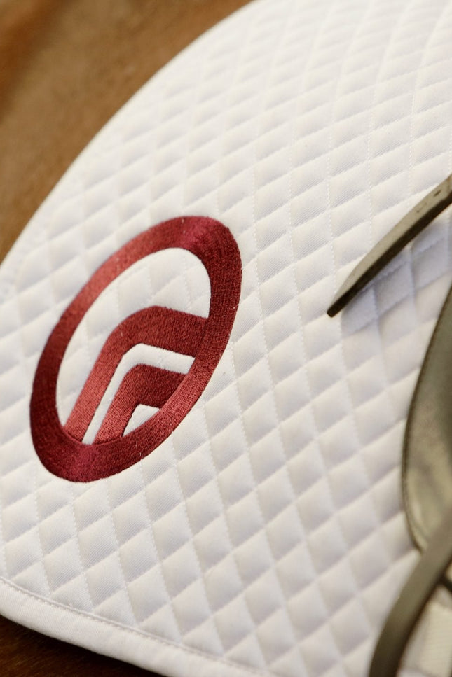 Close-up of a white saddle pad with a red logo on a horse.