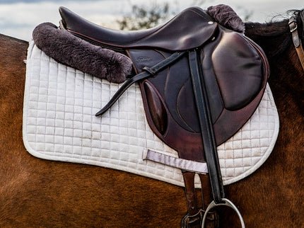 Horse saddle with a white quilted pad on a horse, with a blurred natural background.