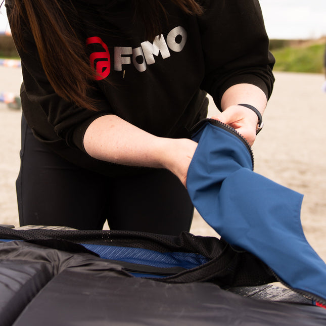Person wearing a black sweatshirt with 'FOMO' logo, interacting with a blue jacket on a blurred outdoor background.