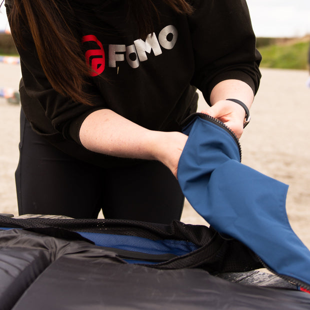 Person wearing a black sweatshirt with 'FOMO' logo, interacting with a blue jacket on a blurred outdoor background.
