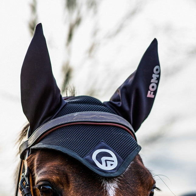 Horse wearing a black fly veil with visible branding, against a blurred natural background.