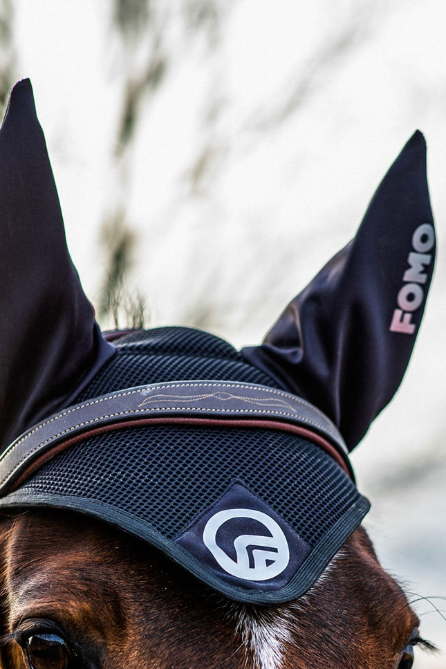 Horse wearing a black fly veil with visible branding, against a blurred natural background.