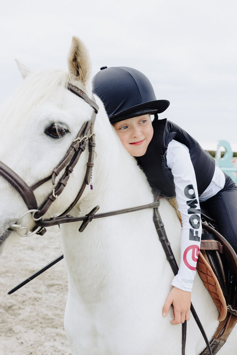 Person in equestrian attire sitting on a white horse with a blurred background