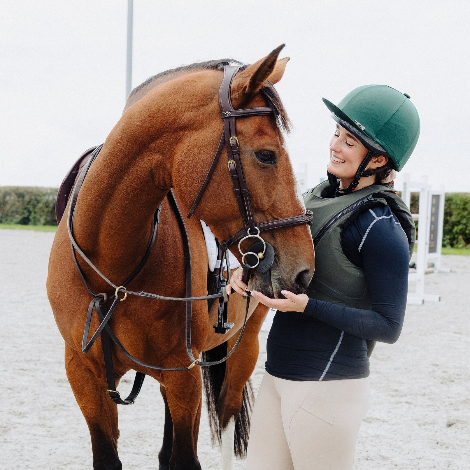 Person in equestrian attire standing next to a horse on a gravel surface.