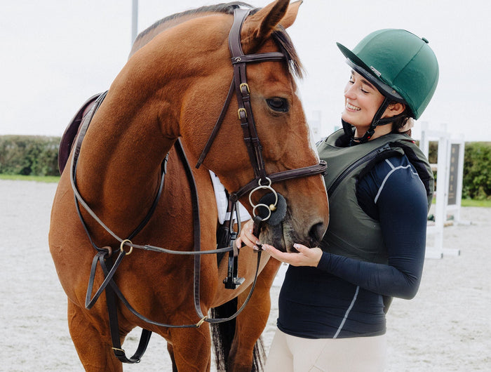 Person in equestrian attire standing next to a horse on a gravel surface.